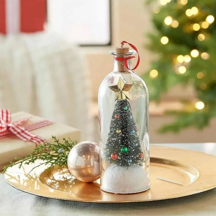Star-topped tree inside a Christmas bottle ornament on a tray with a bauble and gift