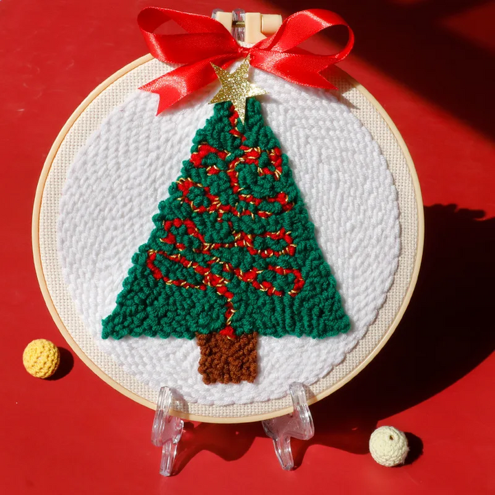 Christmas tree punch needle hoop with red garlands, a white background, and a red ribbon
