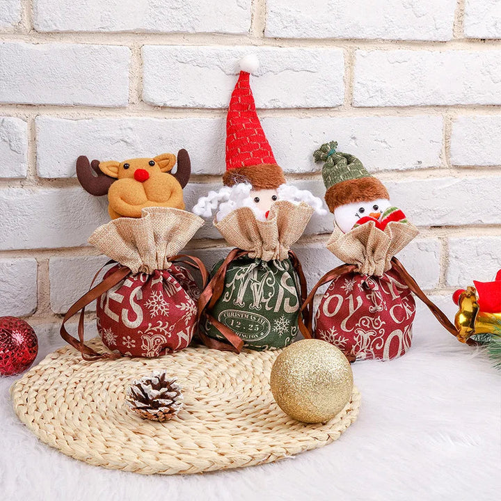 Reindeer, elf, and snowman gift bags with gathered beige tops, displayed beside Christmas ornaments.