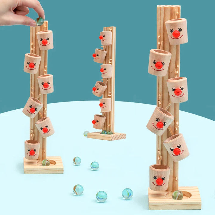 Hand placing a marble in a top cup, with three wooden clown towers shown