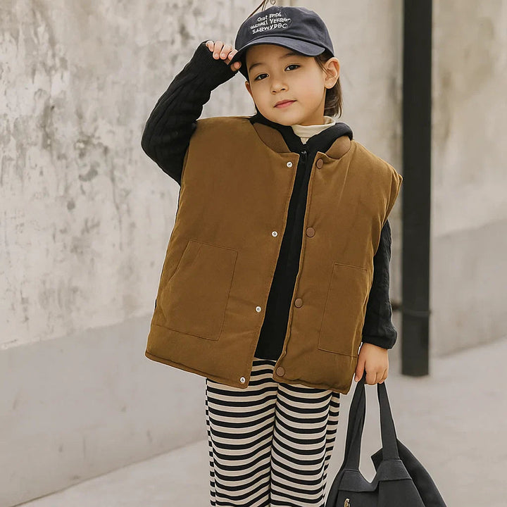 Child wearing a coffee brown vest over a black hoodie with striped pants.
