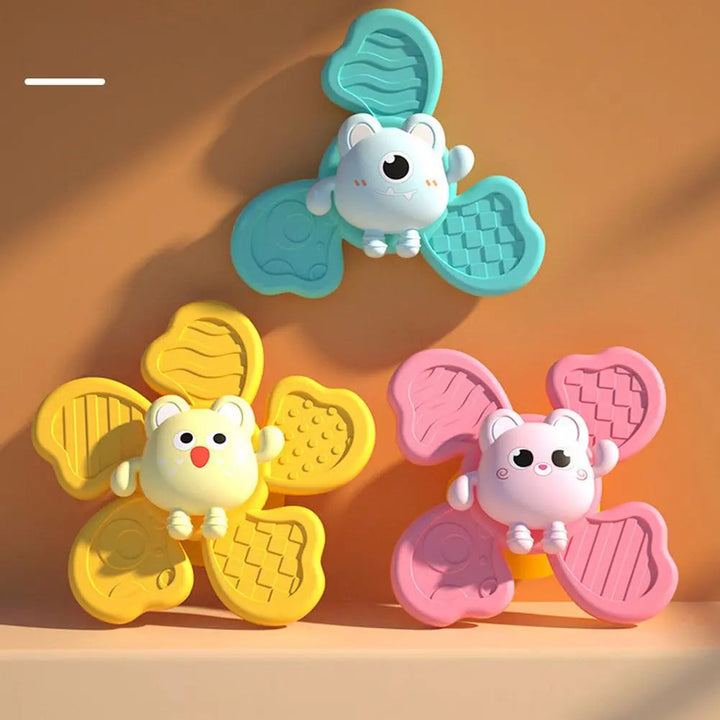 Blue, yellow, and pink animal bath spinners with textured paddles displayed on a ledge.