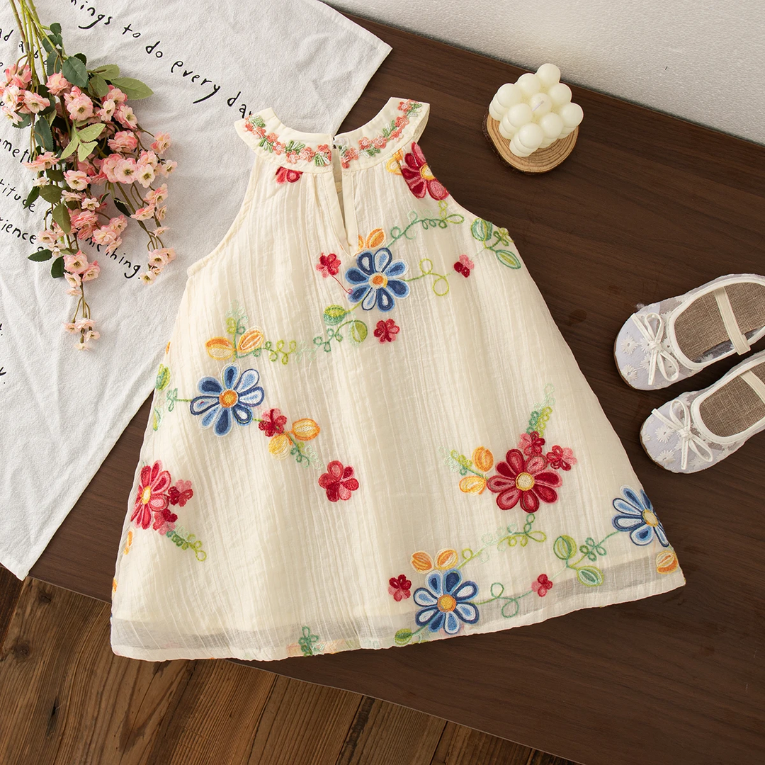 Cream summer dress with bright floral embroidery across the skirt, laid flat on a wooden surface