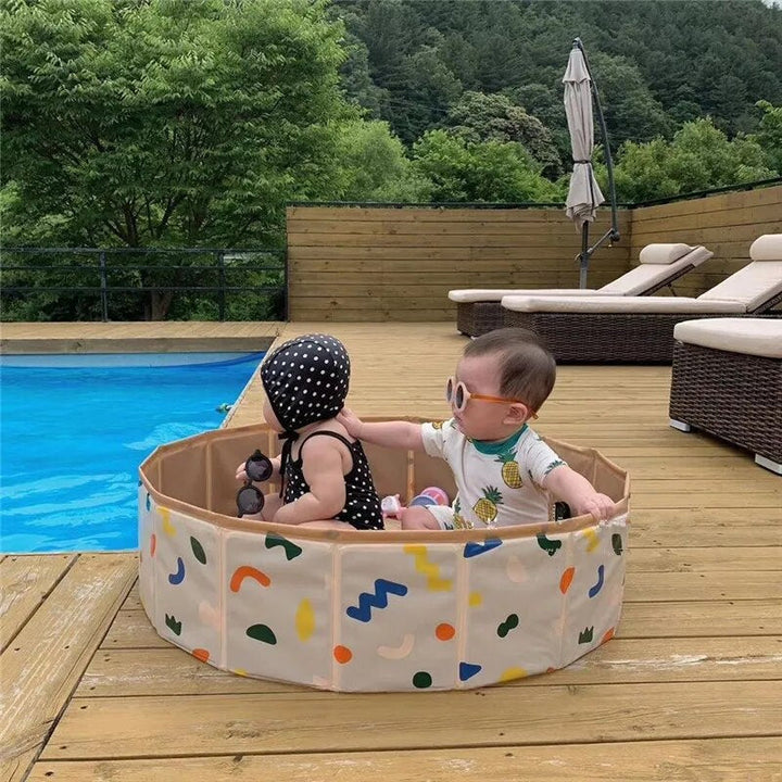 Two children sitting in a colorful round play pool on a wooden poolside deck