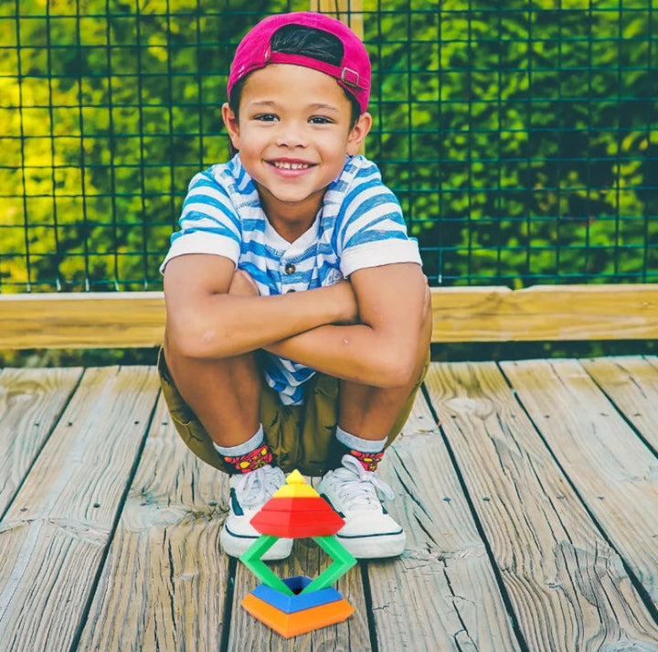 Child crouching on a wooden deck behind a multicolored block tower