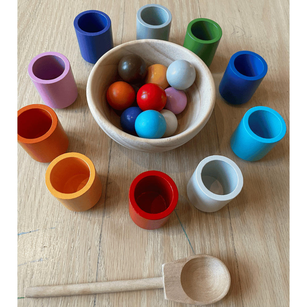 Colorful wooden cups arranged around a bowl of matching balls, with a wooden spoon