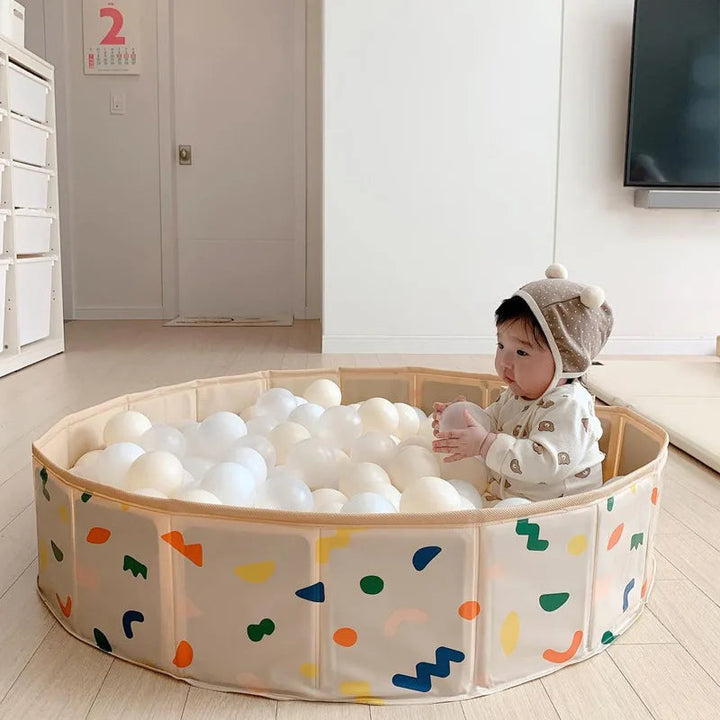 Baby sitting among white play balls in a round, multicolored play pool indoors