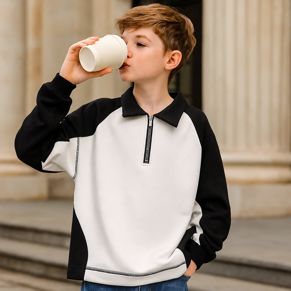 Child wearing the white and black collared sweater while drinking from a cup.