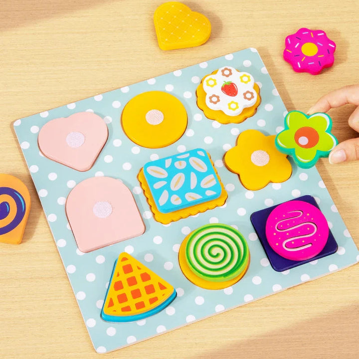 Hand holding a flower-shaped cookie beside a wooden cookie matching board