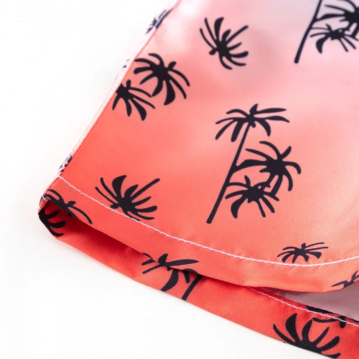 Stitched hem on coral and pink swim trunk fabric with black palm tree prints.