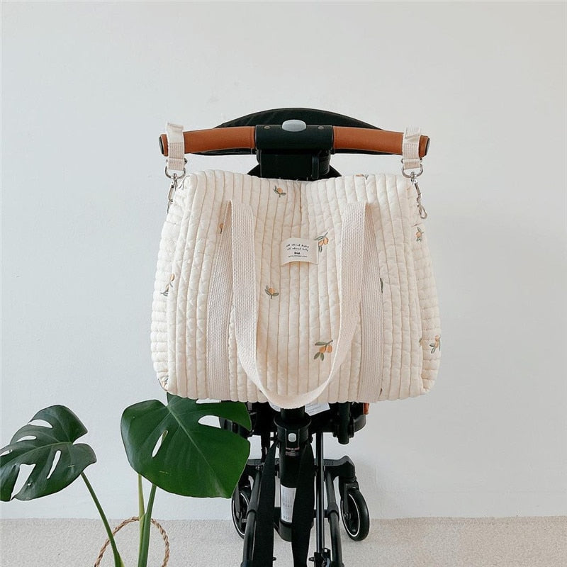 Printed cotton diaper bag hanging from a stroller handle with two attachment straps