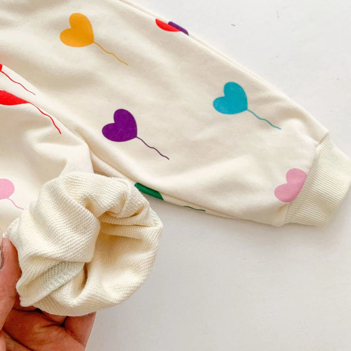 Close-up of colorful heart balloons and ribbed cuffs on the cream cotton baby tracksuit