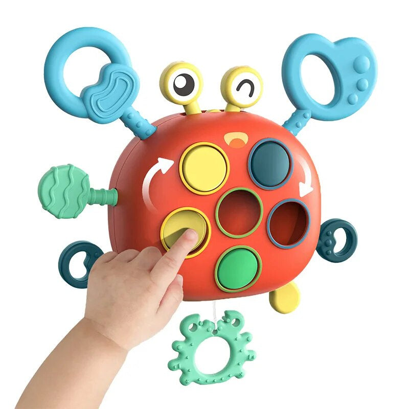 Red crab-shaped sensory toy with blue rings, colored circles, and a hand pressing a yellow circle