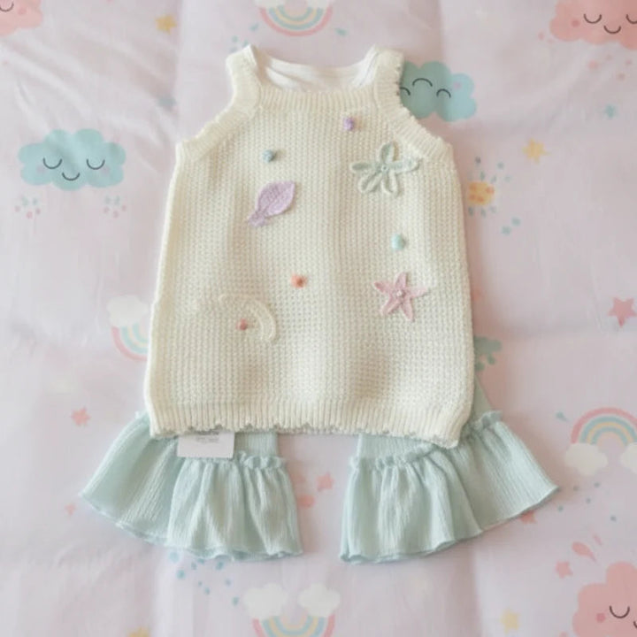 Cream appliqué knit top laid over pale green pants with ruffled hems