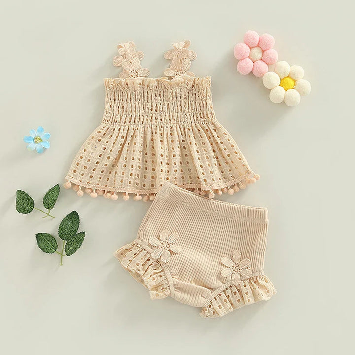 Cream baby outfit with a floral-strap top and matching ribbed shorts laid out with flower decorations