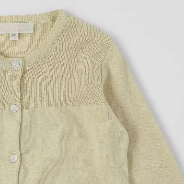 Close-up of a cream knit cardigan with a round neckline, buttons, and textured yoke