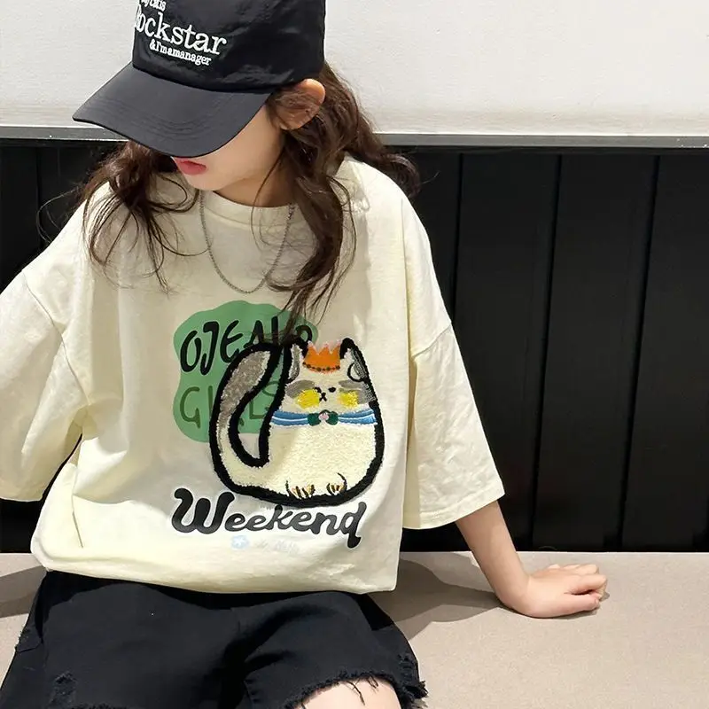 Seated child wearing the cream cartoon-cat T-shirt with black shorts
