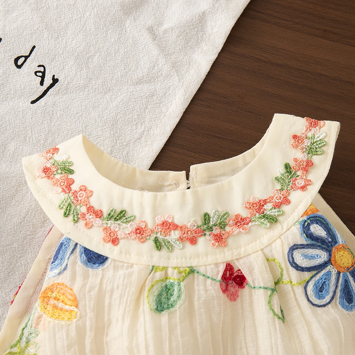 Close-up of pink and green floral embroidery on the rounded collar of the cream dress
