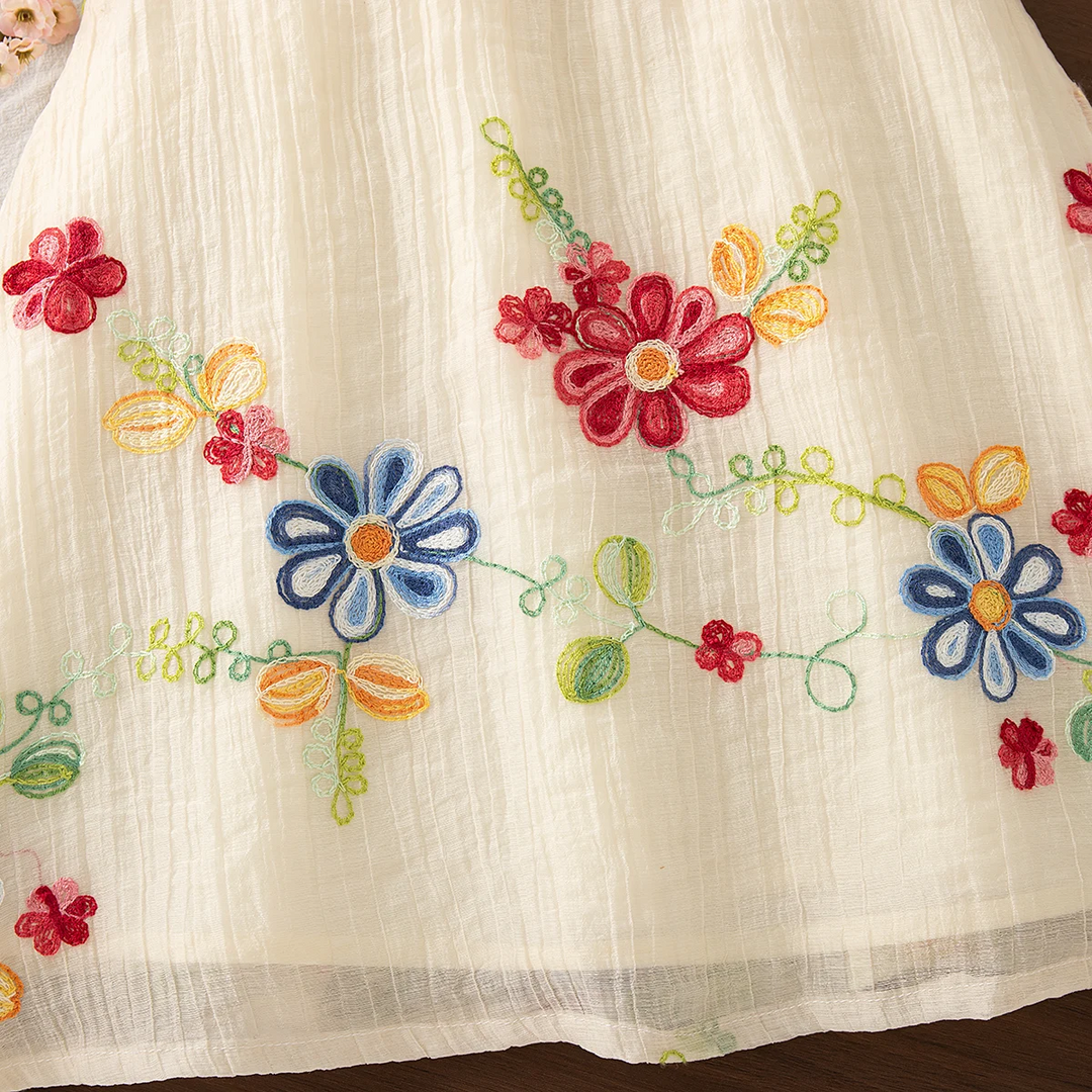 Red and blue embroidered flowers with green stems across the cream dress skirt