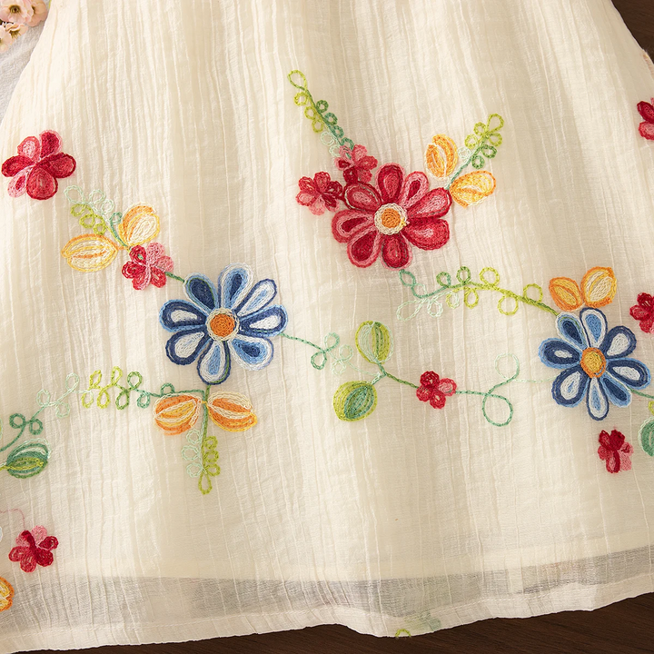 Red and blue embroidered flowers with green stems across the cream dress skirt