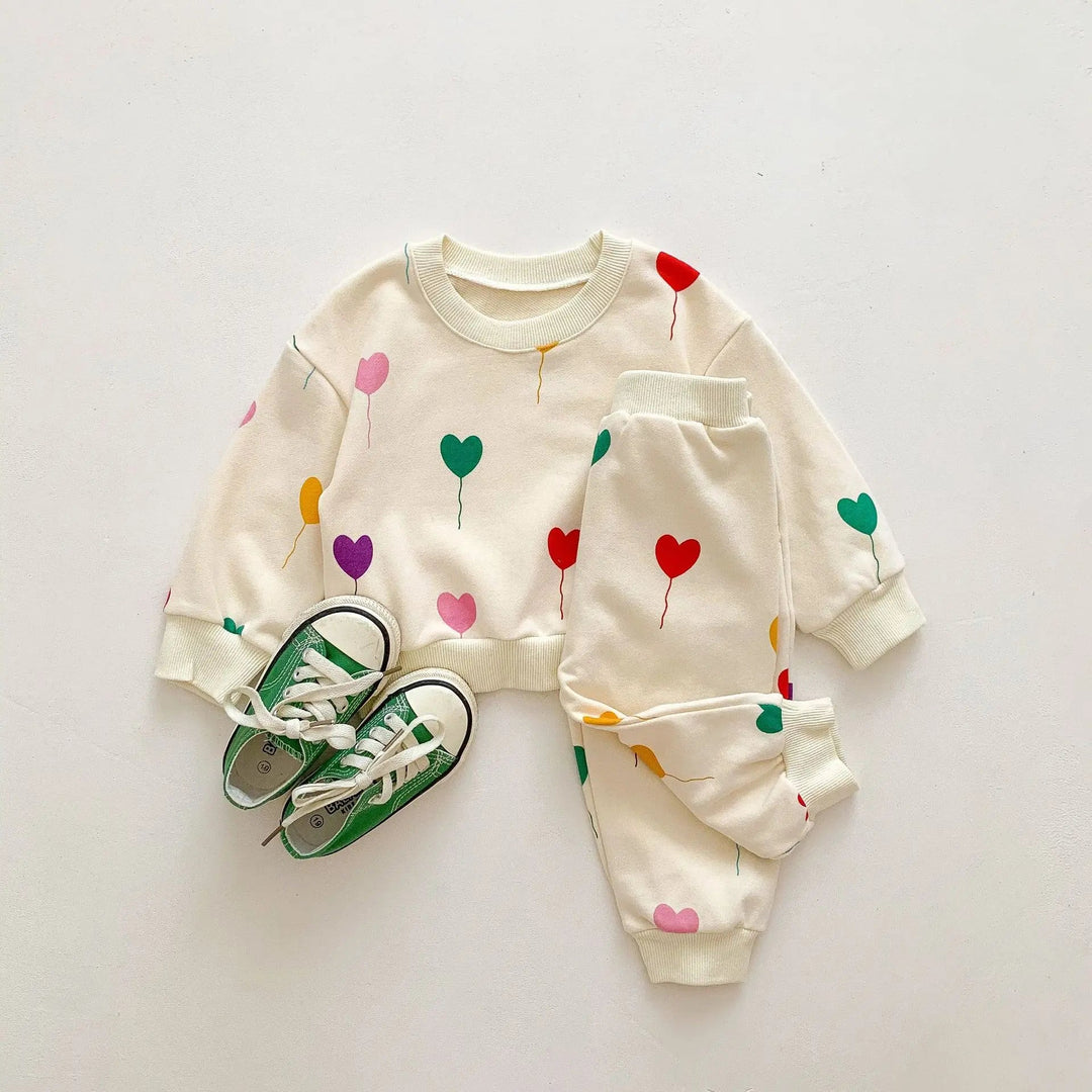 Cream heart-print baby sweater and pants styled with green sneakers