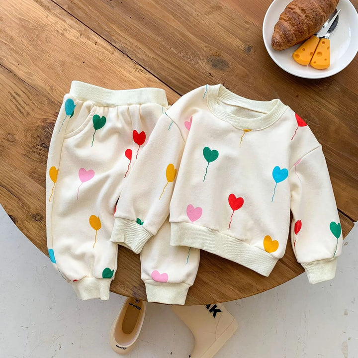 Cream baby sweater and matching pants with colorful heart balloons on a wooden table