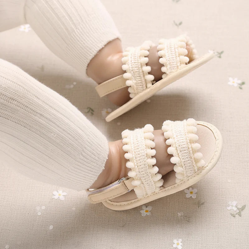 Close-up of cream pom-pom sandals worn with white baby leggings.