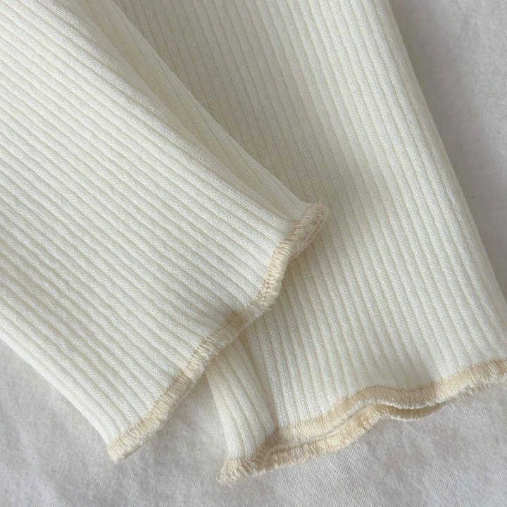Close-up of cream ribbed pant legs with wavy hems