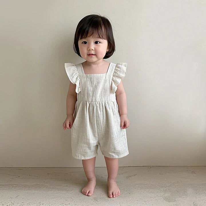 Front view of a child wearing a cream romper with ruffled shoulder straps and short legs.