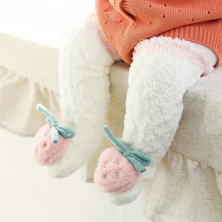 Baby wearing cream long socks with pink cuffs, strawberry toes, and green bows.