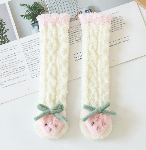 Cream long baby socks with strawberry toes, green bows, and pink cuffs on an open book.