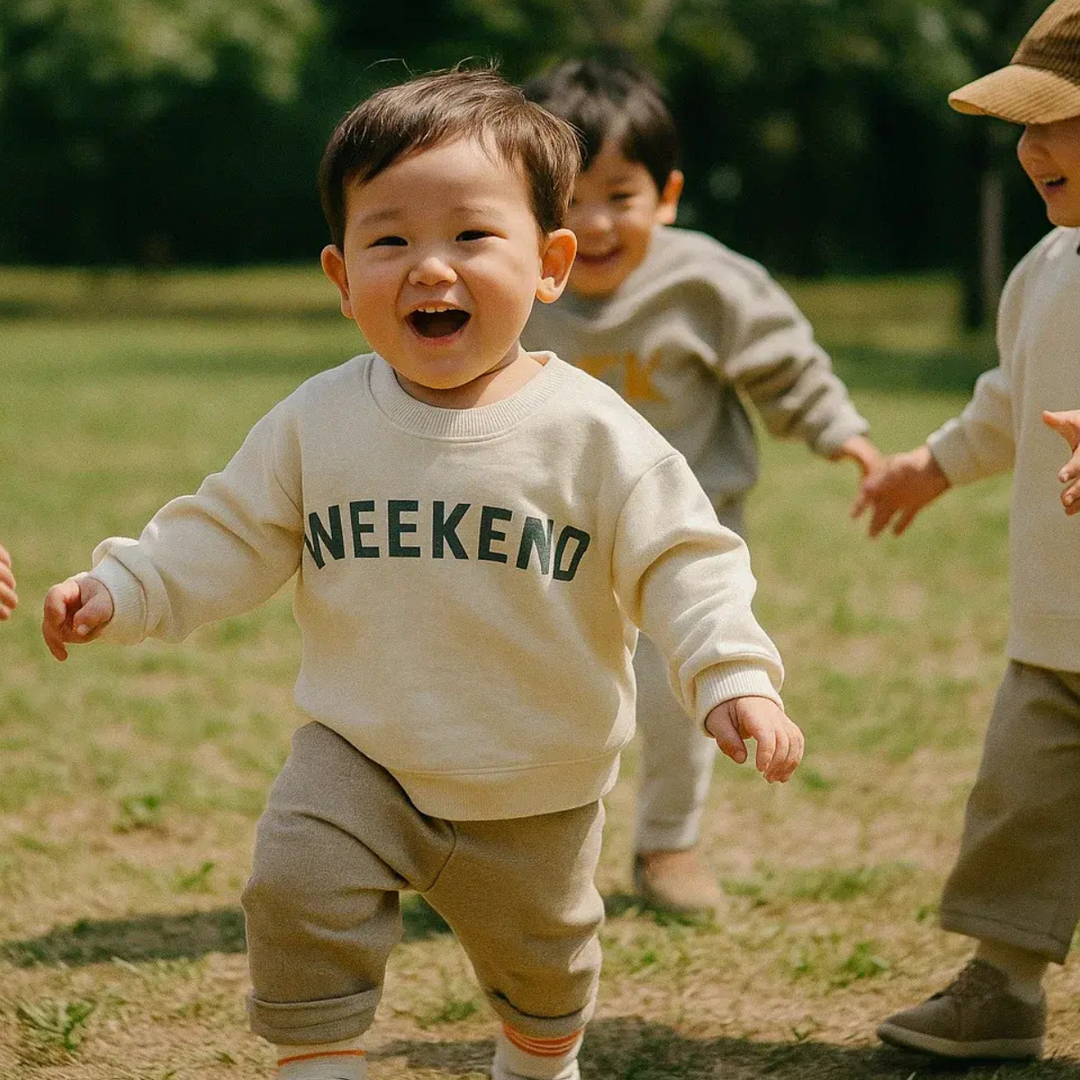 Child running on grass in a cream Weekend sweater with other children behind.