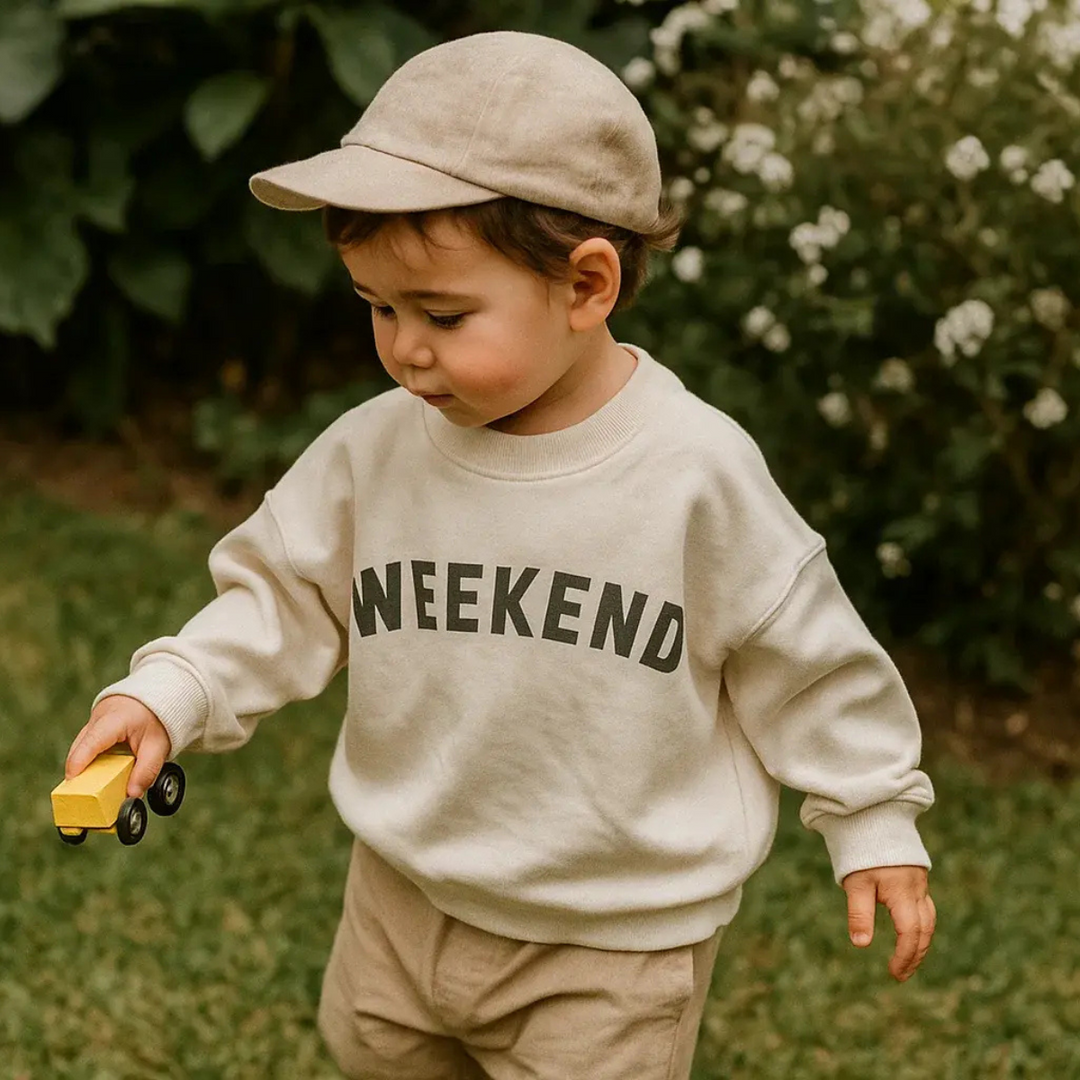 Child wearing a cream sweater and beige cap while holding a yellow toy truck.