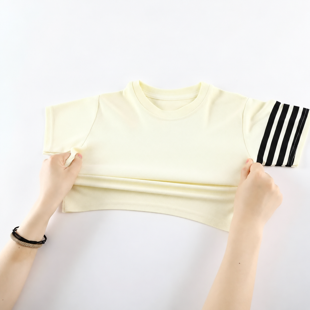 Hands pulling the lower front of a cream T-shirt with black stripes on one sleeve.