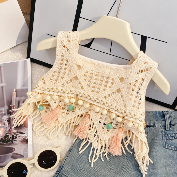 Close-up of the cream crochet-style top with geometric openwork, fringe, and pastel tassels
