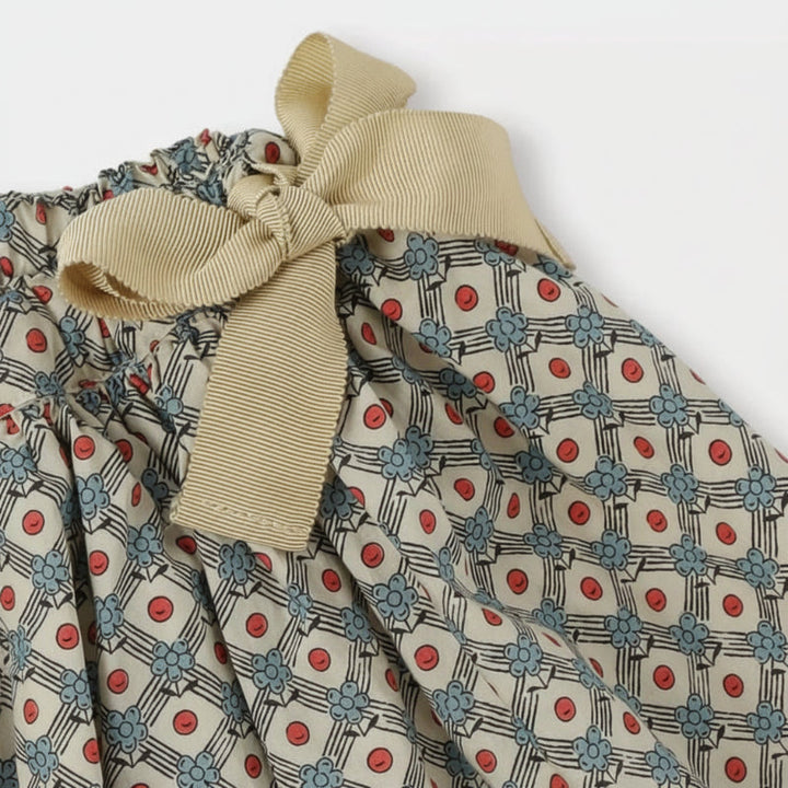 Beige bow at the gathered waistband of the daisy-print skirt