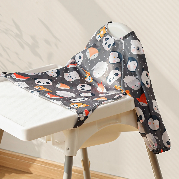 Dark animal-face-print baby bib with long sleeves spread over a high-chair tray