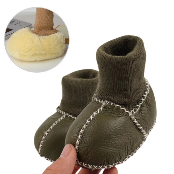Dark green baby slippers held in a hand, with matching knit cuffs and contrast stitching