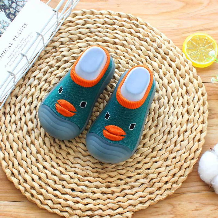 Dark green duck-face sock shoes with orange trim on a woven mat
