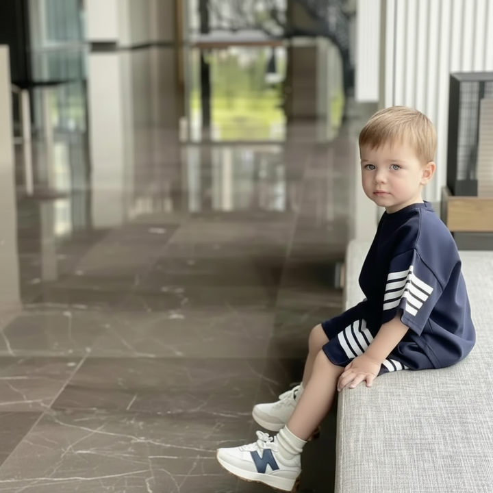 Child wearing the dark striped T-shirt and shorts set while seated on a bench.