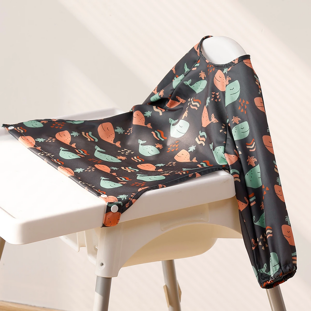 Dark whale-print baby bib showing its wide front and long sleeves on a high chair