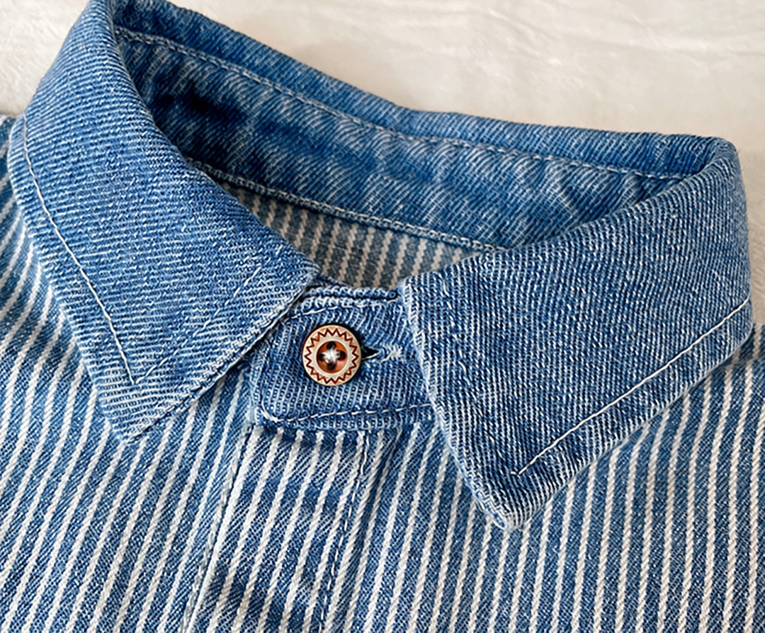 Close-up of the denim fold-over collar, top button and blue and white striped fabric.