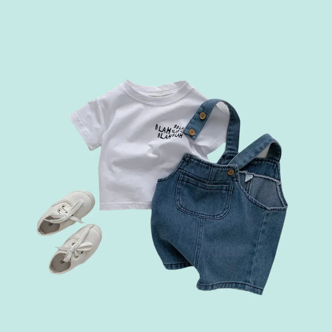 White graphic T-shirt and blue denim short overalls styled with white shoes on a mint background