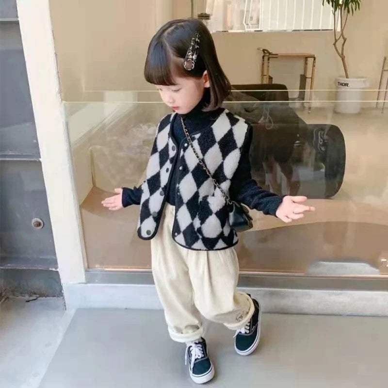 Child wearing a black-and-white diamond-check vest over a dark top with cream pants