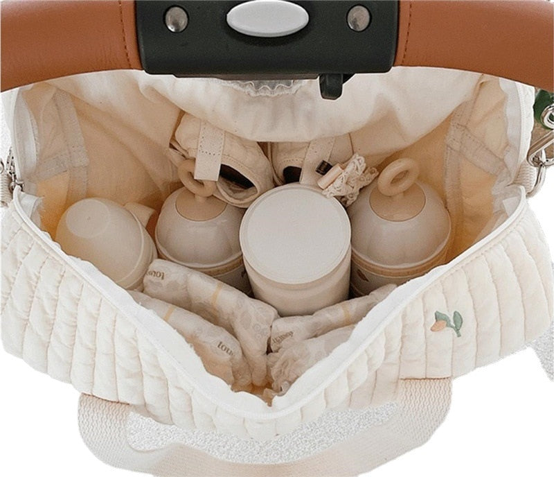 Open quilted diaper bag attached to a stroller, with bottles arranged in interior compartments