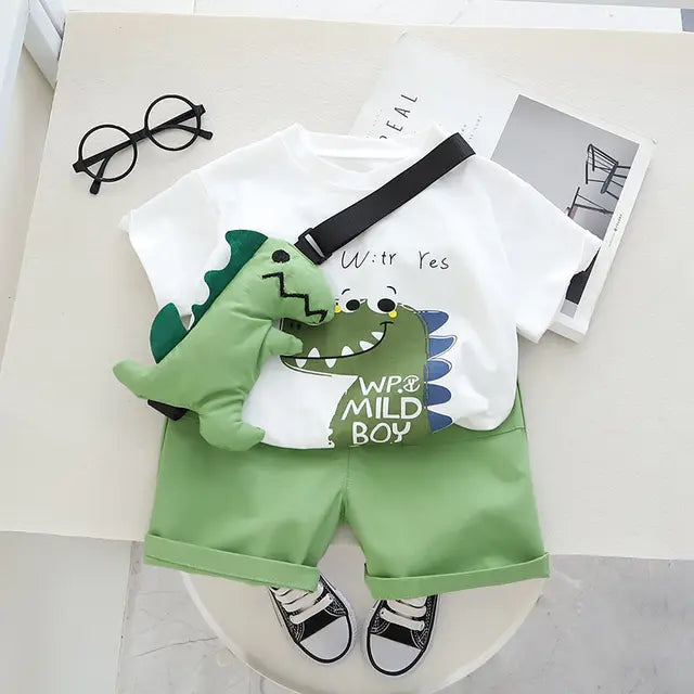 Dinosaur-print cotton T-shirt, green shorts and dinosaur toy with black strap arranged flat