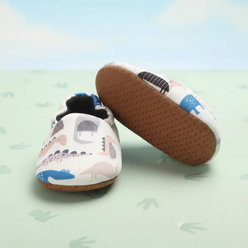 Dinosaur-print baby shoes with one shoe turned to show the textured brown sole.