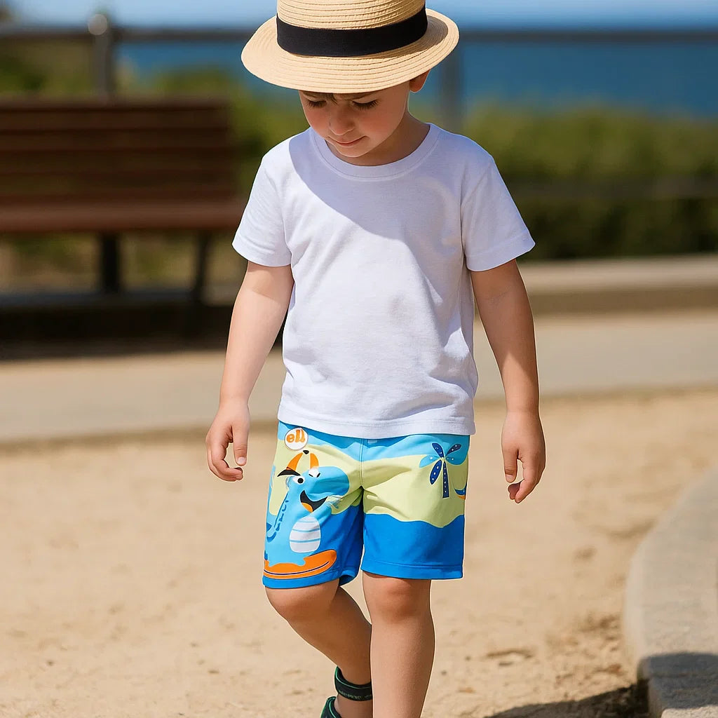 Child wearing blue dinosaur-print swim trunks, a white T-shirt, and a straw hat outdoors.