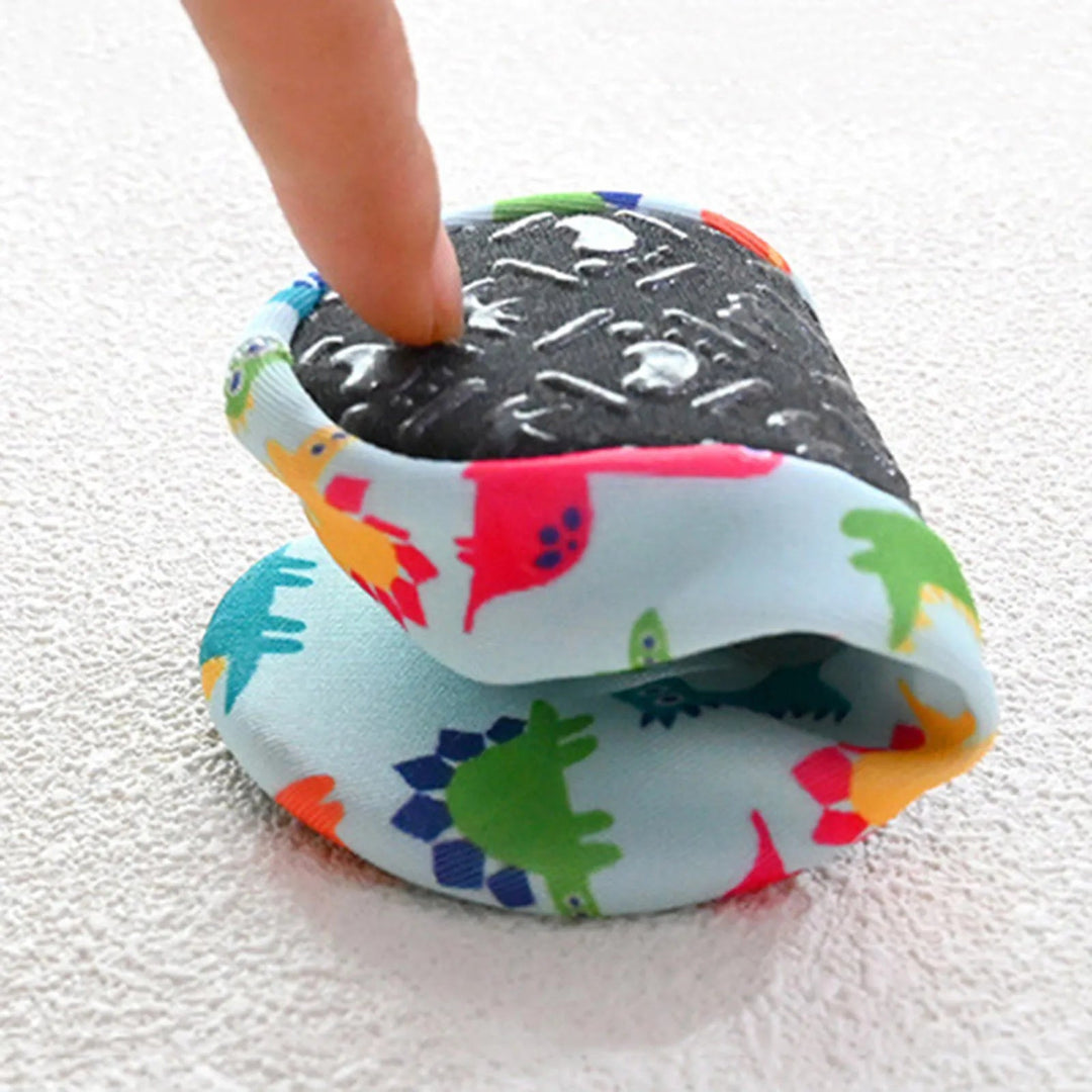 A hand bends a dinosaur-print water shoe to show its flexible sole