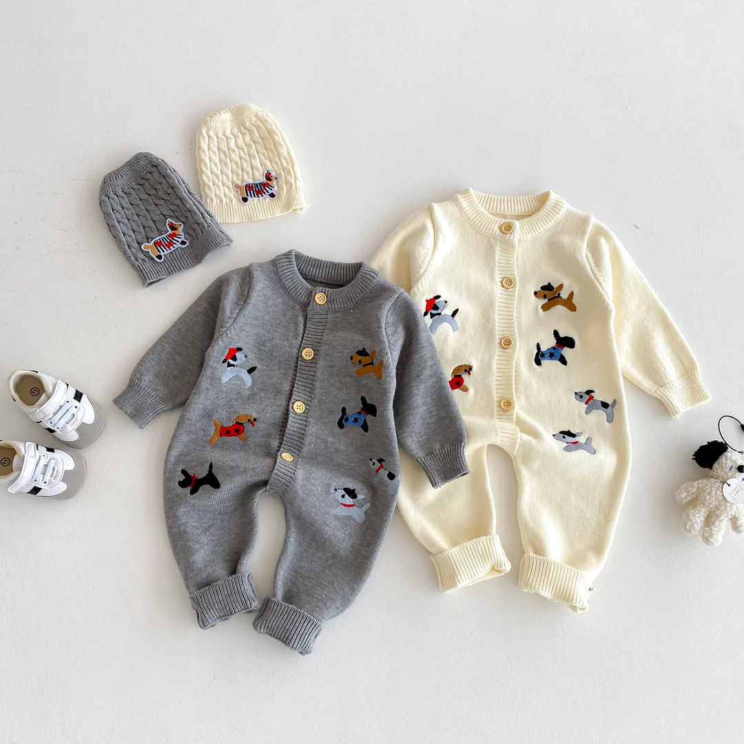 Gray and beige dog-pattern baby jumpsuits laid flat beside knitted hats